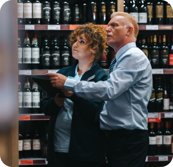 Two retail staff members reviewing inventory data on a tablet while standing in front of stocked wine shelves.