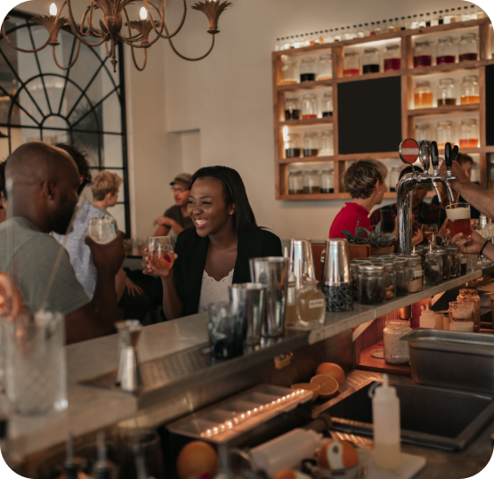 Customers seated at a bar counter with beverages while drinks are being served at a bar service station.