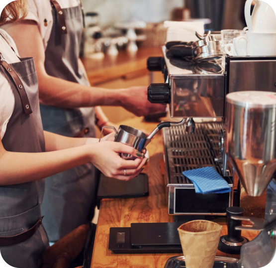 Cafe staff preparing beverages at an espresso machine station with coffee equipment and preparation tools.