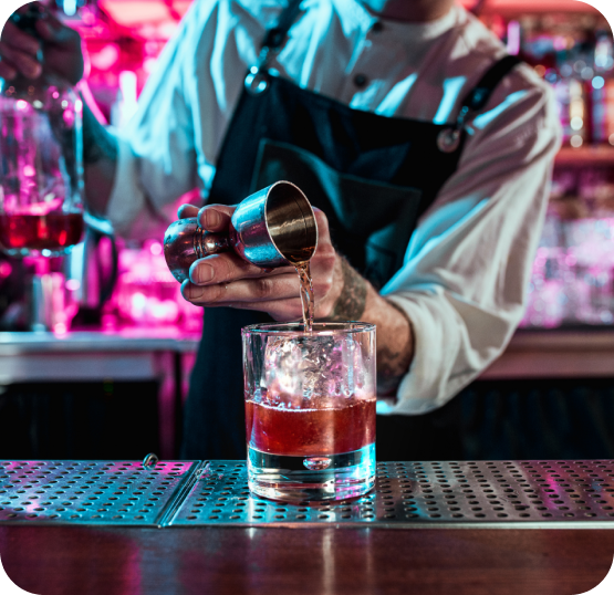 Bartender-style drink preparation with a cocktail being mixed and poured into a glass at a bar counter.