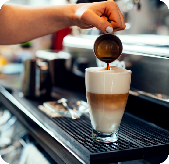 Coffee beverage being prepared as espresso is poured into a layered latte at a café workstation.