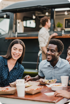 Guests enjoying meals at an outdoor dining table beside a food truck.