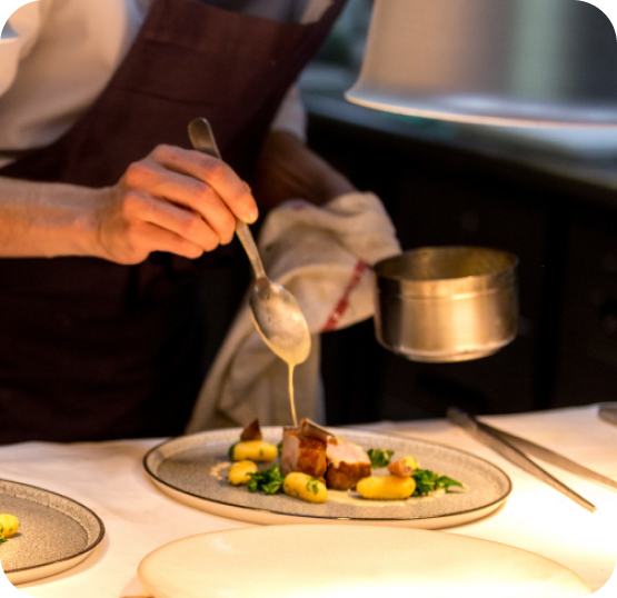 Restaurant staff member plating and finishing a prepared dish before service.