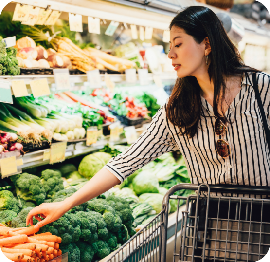 Customer selecting fresh produce from a grocery store display while shopping with a grocery cart.